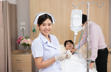 Asian woman nurse checks the saline bag and doctor man checking the patient on bed in the hospital....