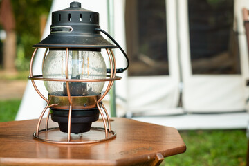 Close up Beautiful vintage camping brass lantern on a wooden tablewith a background of tents in the camping,Relaxing in the midst of nature