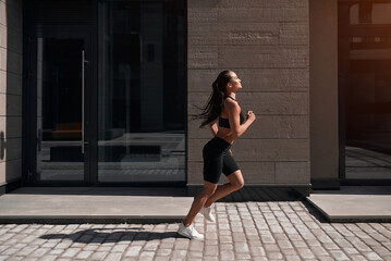 Fototapeta premium Young athletic woman running in the city, shot of girl jumps on the glass building background.