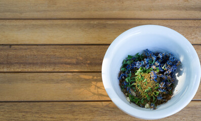 Lavender bloom, cinnamon powder, and mint leaves in a white bowl with wood background and space  for text