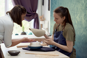 Young skillful pottery master teaching apprentice sculpting mud bowl in creative art studio