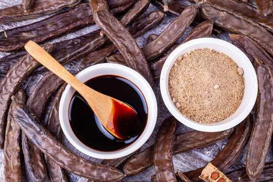 Carob molasses and carob pods on wooden background