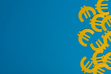 Paper yellow symbols of euro currency on blue background. View from above with copy space.