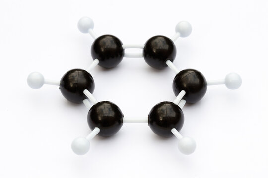 Plastic ball-and-stick model of a benzene molecule (C6H6) on a white background. The molecule is shown with kekule structure. Shallow depth of field.