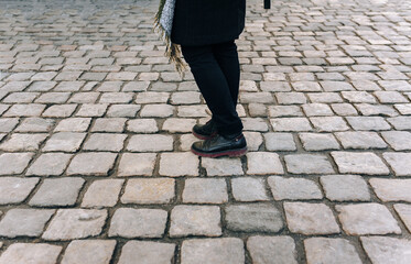 Women's legs in black jeans and winter boots walk along gray granite paving stones. The concept of a walk in the old city.