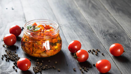 Sun dried tomatoes in glass jar with ripe tomatoes on dark wooden background, selective focus, copy space