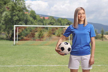 Female soccer player holding a ball under arm on a football pitch