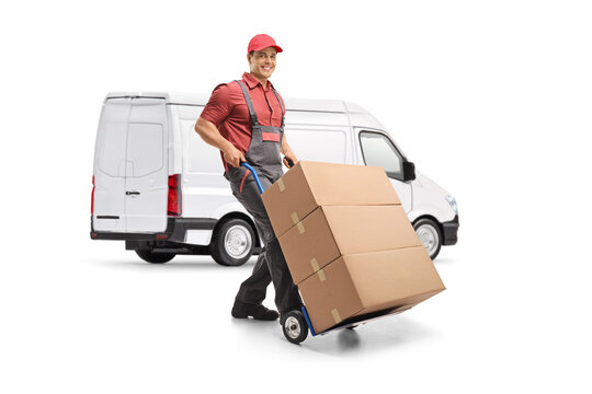 Male worker in a uniform pushing a hand truck loaded with boxes in front of a white van