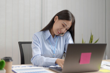 Young Asian woman typing and talking on the phone at the same time.