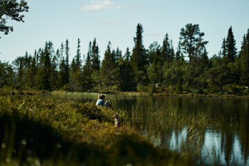 A young girl fishes at a beatiful lake in the deep and wild forest of Norway. Alone in the relaxing nature.