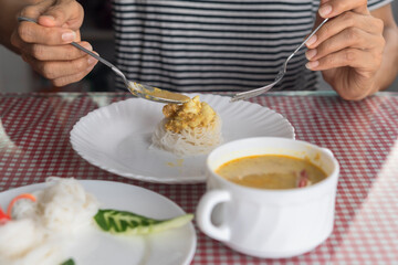 People using spoon and fork eating Thai curry noodle in restaurant