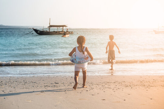 Small girl and boy running to the ocean from the beach in Bali