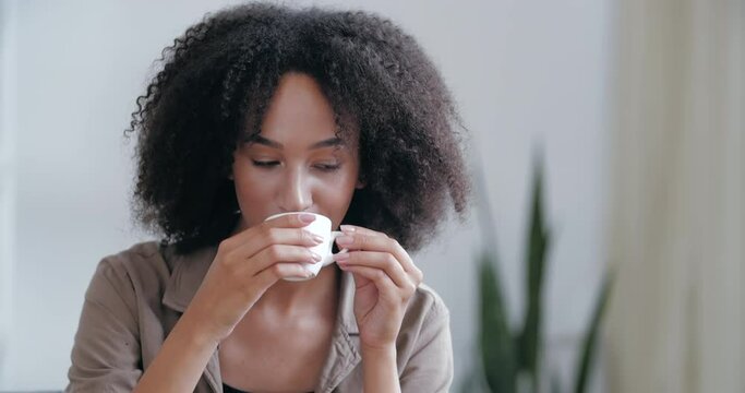 Smiling Happy African American Woman Sitting On Sofa In Casual Clothes, Picking Up Hot Cup Of Coffee, Drinking Delicious Latte, Using Laptop For Video Communication With Friends, Online Conference