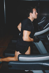 Fototapeta na wymiar Attractive sportsman at the gym doing exercise on the treadmill, handsome brunette man doing workout in gym running fast on a treadmill, fit man running in a gym on a treadmill looking to the screen