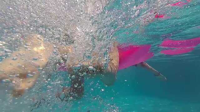 Slow motion footage of two girls swimming, holding on to a pink rubber mattress, underwater shot