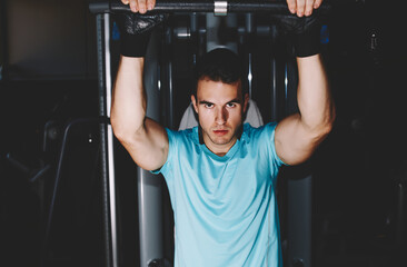 Fototapeta na wymiar Muscular build man exercising on pulls up machine at gym