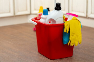 Various household cleaning detergents and bottles in a plastic bucket on the floor