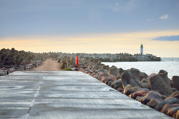 An empty pedestrian walkway (promenade) to the lighthouse at sunset. Breakwaters close-up. Baltic...