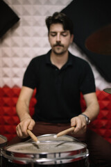 Portrait of man playing on drum set in studio. Blurred drummer holding sticks and playing instrumental music indoor.
