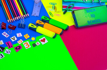 Group of stationery items for back to school - multi colored background,  pencils, notebooks, scissors and text on smart phone - education concept