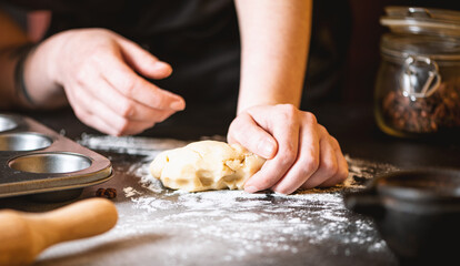 Close-up of a woman in a black apron kneading dough for a pie or cookie. Soft focus.