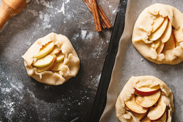 Cooking apple pie. Uncooked Galette with apples on a dark background top view. French cuisine. Sweet autumn food. Homemade baking.