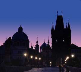 Fototapeta na wymiar Charles Bridge at dawn. Panoramic image, silhouette of Bridge Tower and churches, street lights in Prague, Czech Republic.