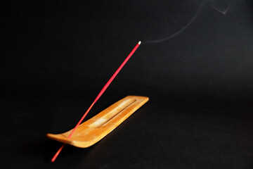 smoking incense stick on wooden stand on black background.