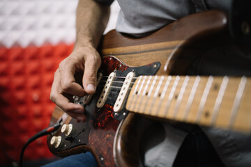 Fototapeta premium Hands of male musician playing electric guitar. Close-up view of cropped male musician playing guitar in soundproof studio.