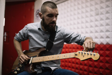 Obraz premium Guitar player setting his music instrument in studio. Rock band member doing rehearsal and setting his guitar before recording audio.