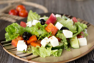 Greek salad on a striped plate on the table in the cafe