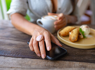 girl with rose quartz ring takes phone on wooden table in cafe.