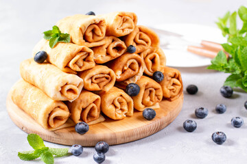 Delicious sweet rolled pancakes with cottage cheese and fruits on a wooden board