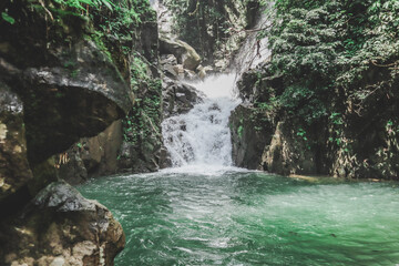 Jungle waterfall cascade in tropical rainforest with rock and turquoise blue pond.