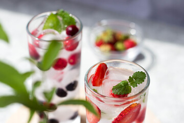 tall glasses full of ice and frozen strawberries and blueberries inside with mint leaves in the sun