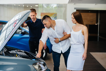 A young couple chooses a new car at the dealership and consults with a representative of the dealership. Used cars for sale. Dream fulfillment
