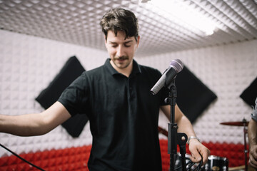 Portrait of smiling man setting microphone on stand. Blurred singer setting cables to his microphone in music room.