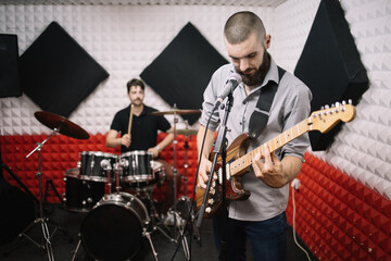 Band of guitarist and drummer rehearsing in studio. Musicians playing and singing on drummer set and guitar in recording music studio.