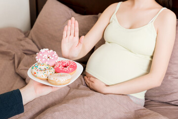 Obraz na płótnie Canvas Close up of pregnant woman staying in bed rejects to eat junk food such as donuts and makes no gesture. Healthy diet for future mother concept
