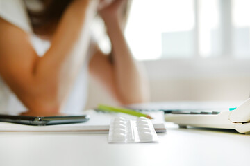 White blisters with pills on working table over blur unemployed depressed woman