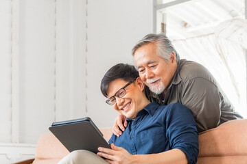 Happy senior asian father and adult son using tablet smartphone in living room