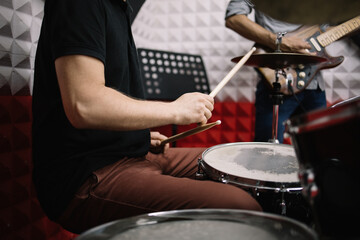 Fototapeta na wymiar Male hands with drumsticks playing on drum set. Cropped drummer playing cymbals and drums and sitting in soundproof room.