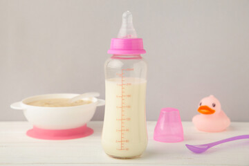 Bowl with baby food with toys on grey background