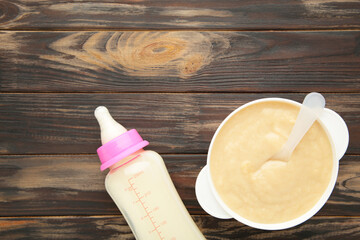 Milk and bowl with porridge for baby on brown background