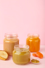 Glass jars with nutrient baby food on pink background