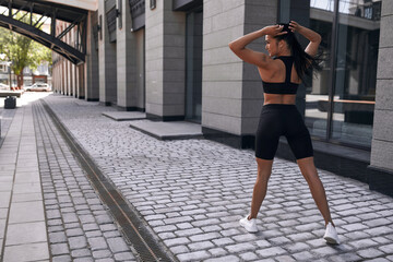 Obraz na płótnie Canvas Beautiful woman, summer in city, fitness training on street, posing against window, sportswear. Background glass windows of a building.