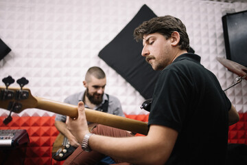 Men holding guitars in soundproof studio. Guitarists facing each other in music recording studio.