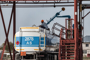 Tank truck on gas filling terminal. Worker on top. Blue sky