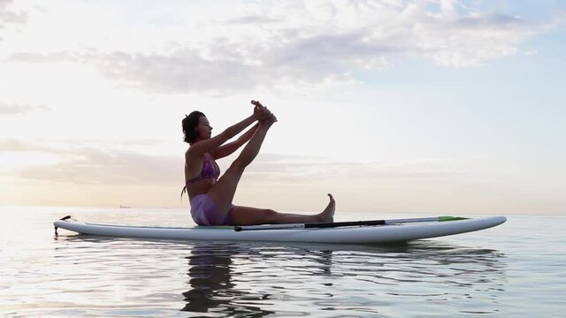Young woman doing YOGA on a SUP board in the lake at sunrise

