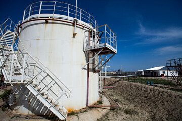White oil storage tank under bright sun on  deep blue sky with light clouds. Oil refinery (oil processing) plant in desert. Near Taraz city, Kazakhstan.